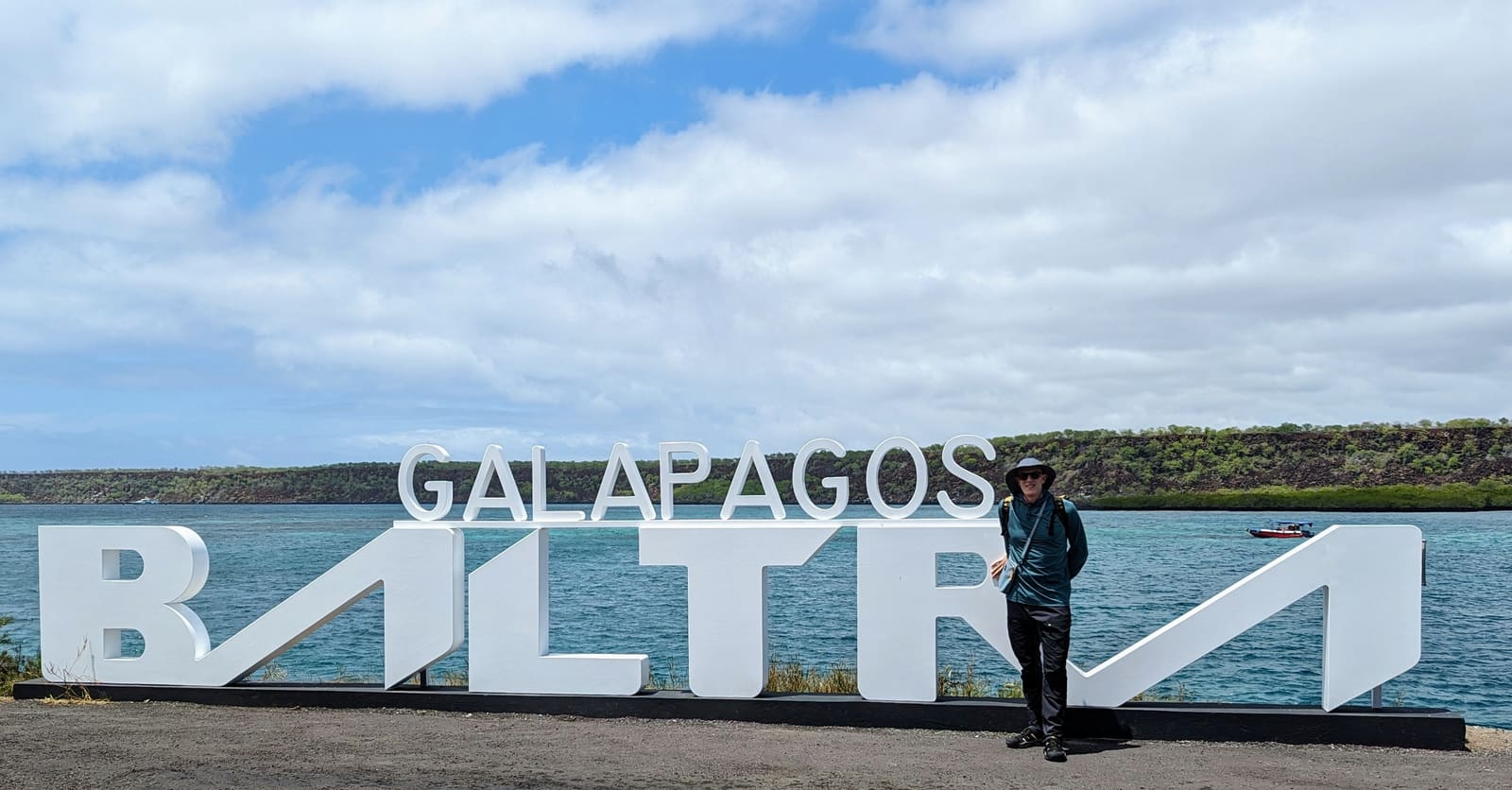 Traveler beside the Galapagos Baltra sign by the water