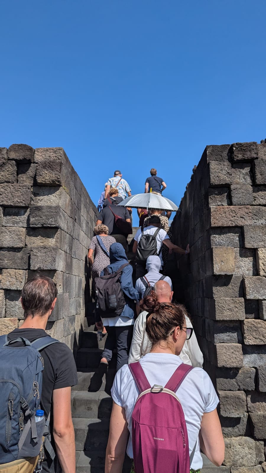 Tourists climbing a narrow stone stairway at Borobudur