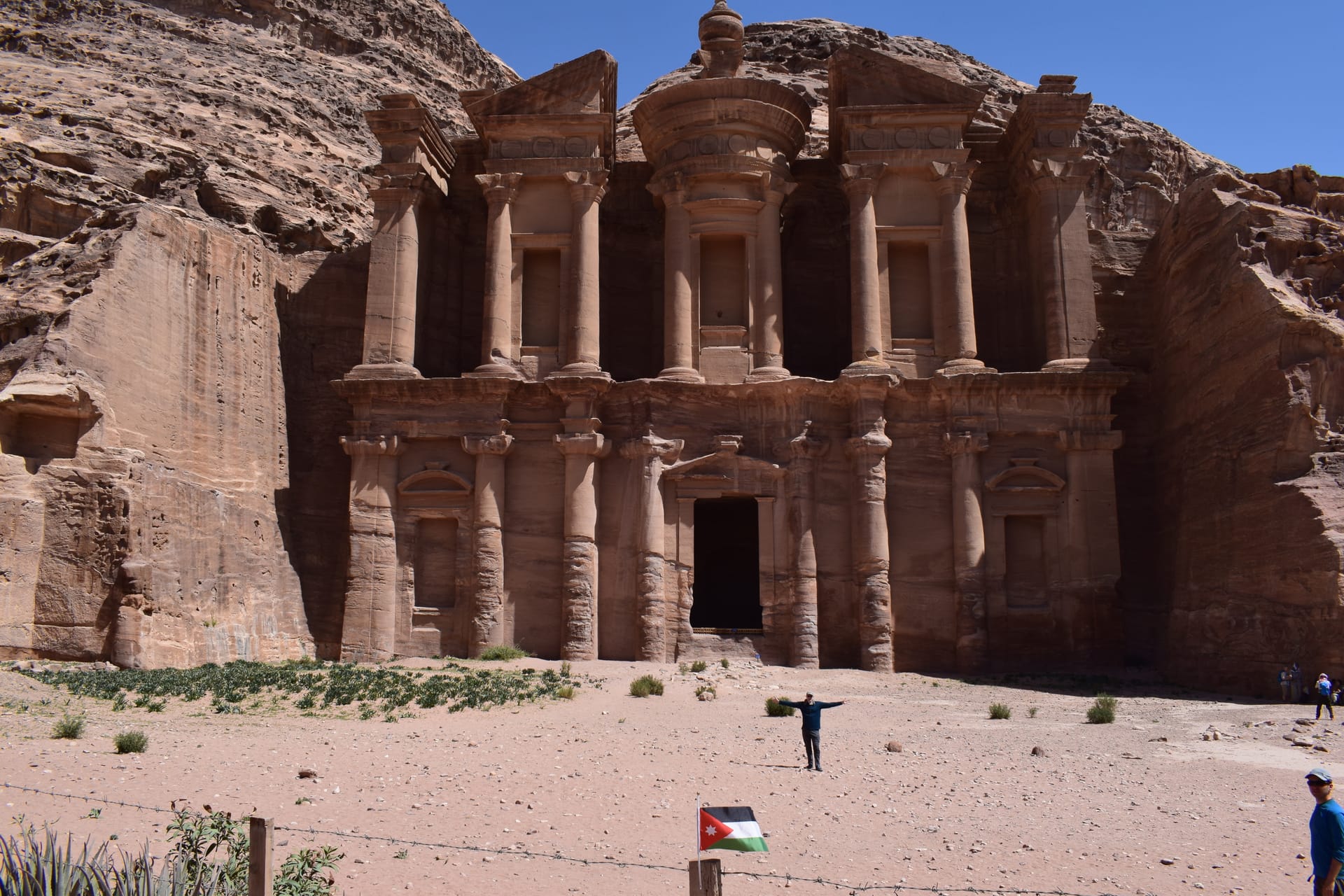 The full sandstone facade of the Monastery at Petra with a Jordanian flag in front