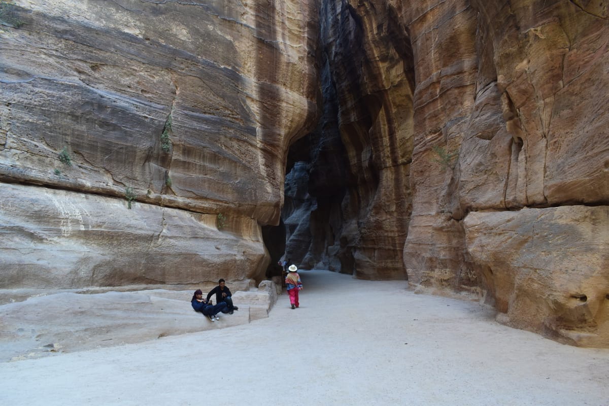 Travelers walking through the narrow rock walls of the Siq at Petra
