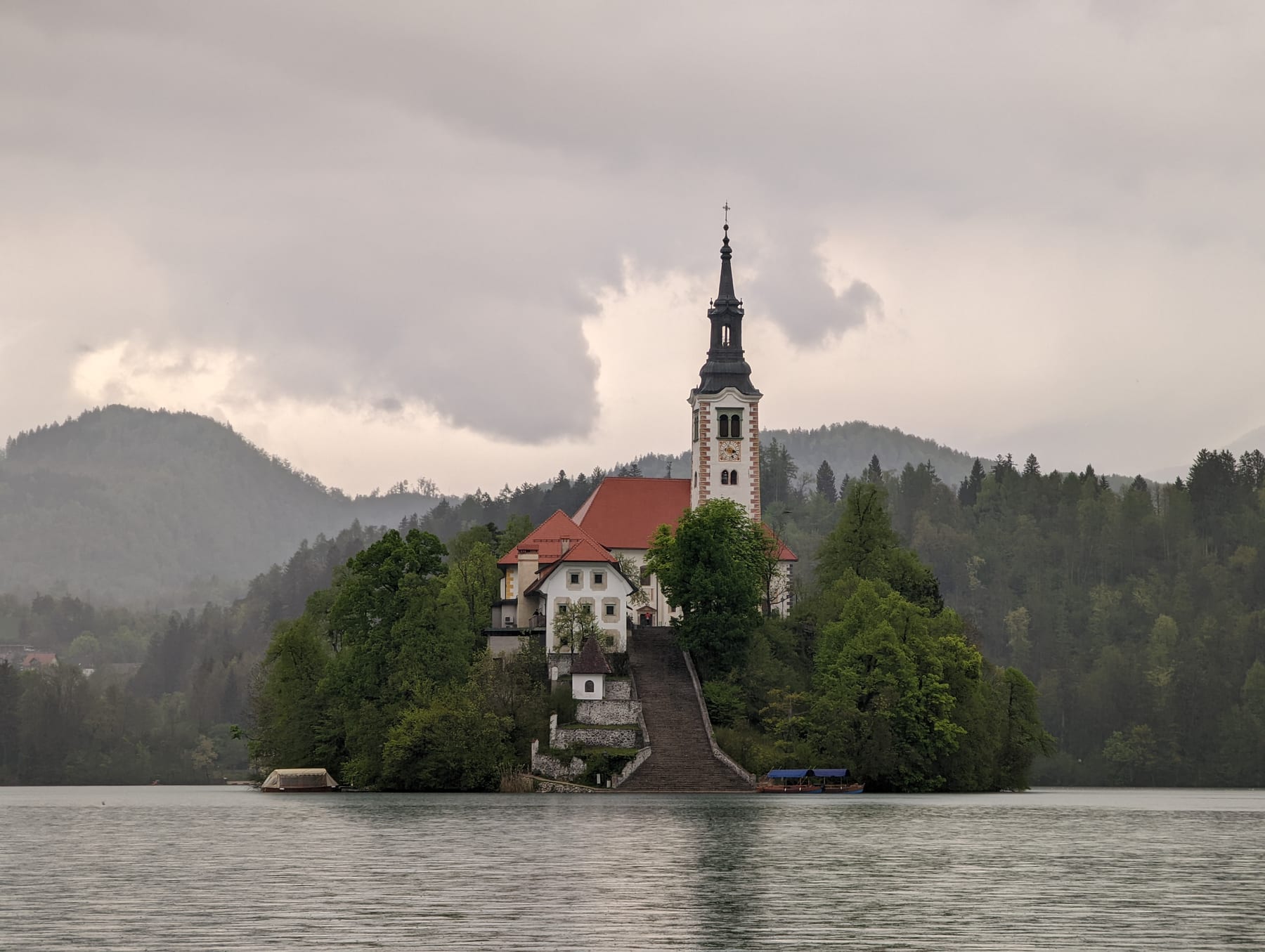 Lake Bled island church beneath low cloud and forested Slovenian mountains