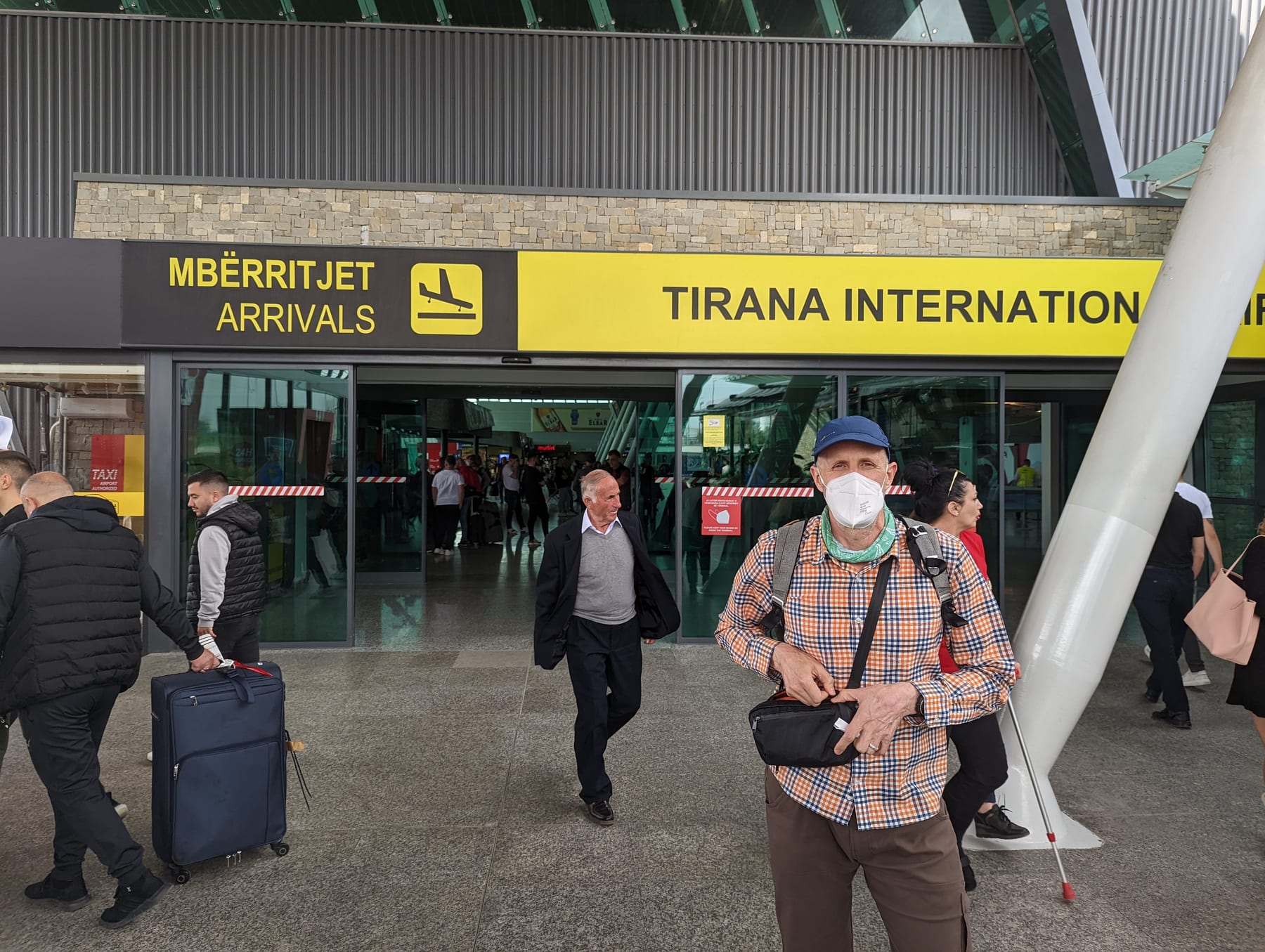 Traveler standing below the Tirana International Airport arrivals sign